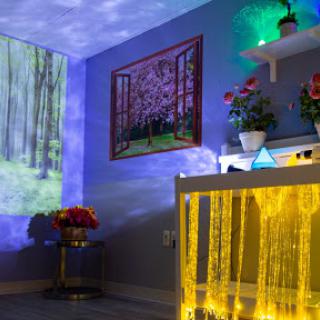 A cozy and vibrant room with ambient lighting, featuring a projector display of a forest scene, floral arrangements, and artistic decorations.
