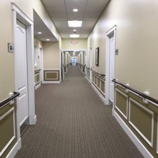 A long, well-lit hallway with carpeted floors, lined with doors and handrails.