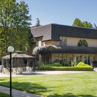 A modern building with a well-maintained garden and outdoor seating on a sunny day.