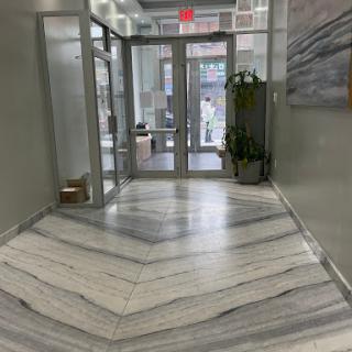 A modern hallway featuring a chevron patterned marble floor and glass entrance doors.