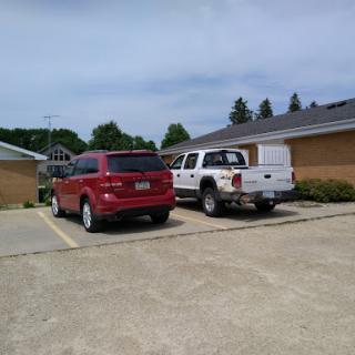 A red vehicle parked next to a white pickup truck in a residential parking lot.