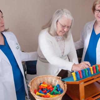 An elderly woman engages in a therapeutic activity with the assistance of two healthcare professionals.