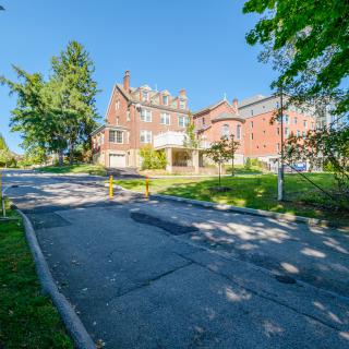 A historic brick building with a pathway, surrounded by trees on a sunny day.
