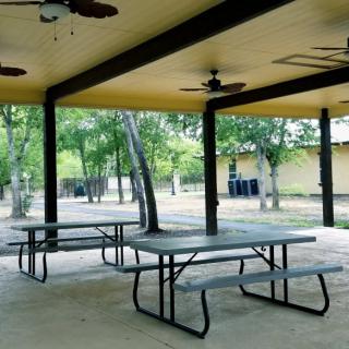 A sheltered picnic area with tables and ceiling fans, surrounded by trees.