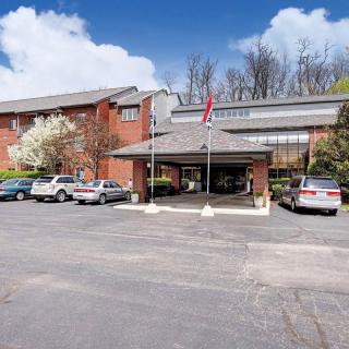 A building with a parking lot and several cars, surrounded by trees under a partly cloudy sky.
