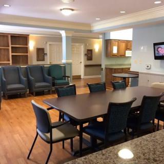 A spacious meeting and dining area with comfortable seating, a large table, and a kitchenette in the background.