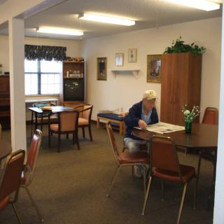 A senior person reading at a table in a quiet community center room.