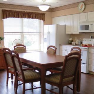A cozy kitchen and dining area with a wooden table and chairs, white appliances, and large windows.