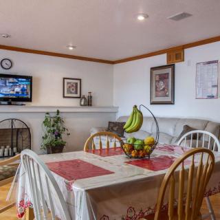 A cozy dining area with a table set for meals, featuring a fruit bowl centerpiece and a TV in the background.