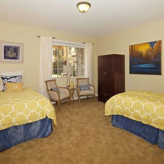 A cozy bedroom featuring twin beds with yellow bedding, two chairs, and decorative artwork on the walls.