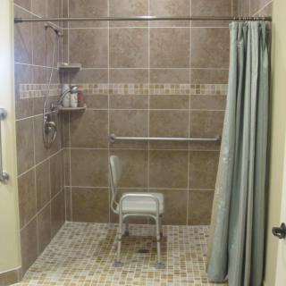 An accessible bathroom with a shower chair, grab bars, and tiled walls.