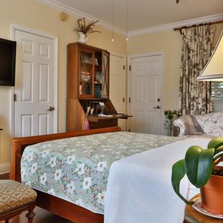 A cozy bedroom interior featuring a wooden bed with floral bedding, a television mounted on the wall, and elegant decor.