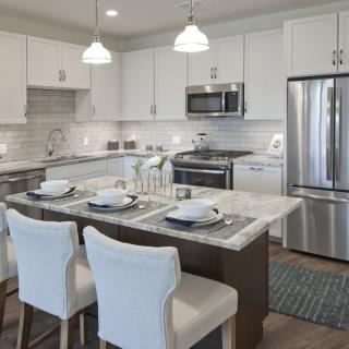 A modern kitchen with white cabinetry, stainless steel appliances, and a stylish kitchen island set for dining.