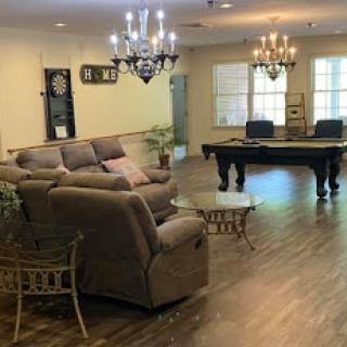 A spacious and elegantly decorated living room featuring a cozy sofa, stylish chandeliers, and a pool table.