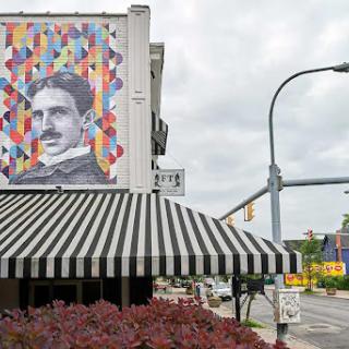 A vibrant mural of Nikola Tesla adorns the side of a building, showcasing street art in an urban setting.