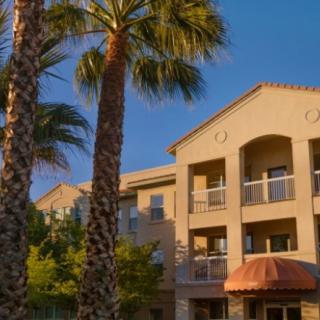 An apartment building with balconies, framed by palm trees at sunset.