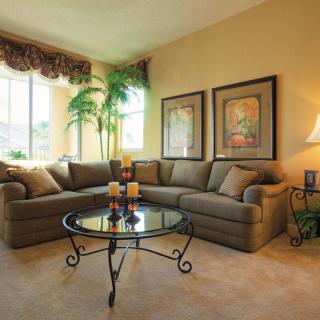 A cozy living room with a large sectional sofa, glass-top coffee table, and decorative elements like artwork and indoor plants.