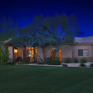 A well-lit house surrounded by trees under a night sky.