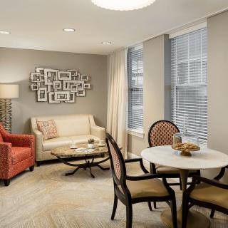 A cozy living room with a sofa and armchair, featuring a small dining area and decorative elements.