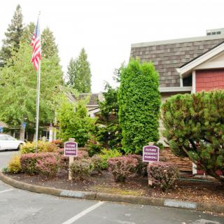 A building with surrounding greenery and a parking lot that includes signs and an American flag.