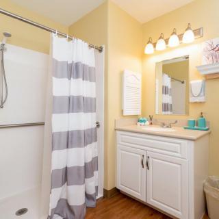 A neat and modern bathroom featuring a striped shower curtain, white vanity with mirror, and bright lighting.