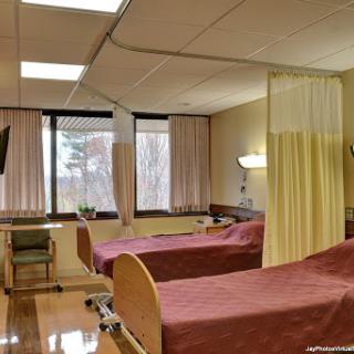A view of a hospital patient room featuring two beds separated by curtains.