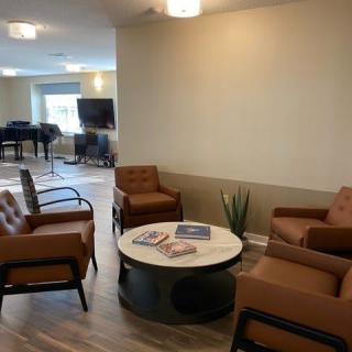 A modern living room with brown armchairs surrounding a coffee table, featuring a piano and television in the background.