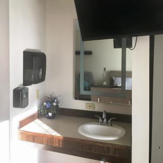 A bathroom with a sink and mirror, featuring a wall-mounted TV and soap dispenser.