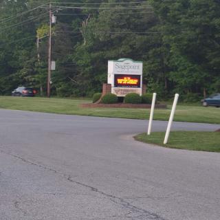 A roadside sign visible from a curve in the road, surrounded by greenery.