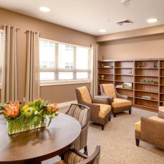 A cozy living room with comfortable chairs, a round table with a flower arrangement, and bookshelves along the wall.