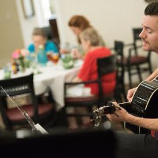 A guitarist performs for people dining indoors.