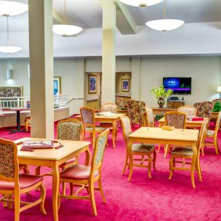 A well-lit dining area with wooden tables and chairs on a red carpet.