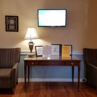 A cozy waiting area featuring a lamp on a wooden table, flanked by two striped chairs, with a television mounted on the wall above.