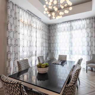 A modern dining room with a sleek black table, patterned chairs, and a striking chandelier.