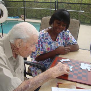 An elderly man playing checkers with a caregiver by the poolside.