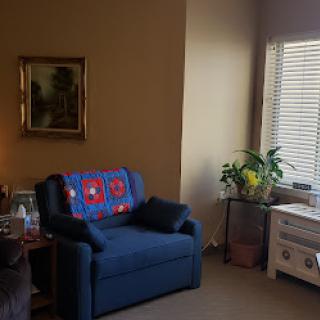 A cozy corner of a living room featuring a blue sofa, houseplants, and artwork on the wall.