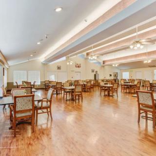 A spacious dining room with multiple tables and chairs, featuring wooden floors and ceiling lights.