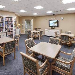 A community room with tables, chairs, bookshelves, and a television.