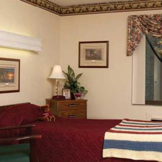 A cozy bedroom with a neatly made bed, a lamp, framed pictures on the wall, and a window with curtains.
