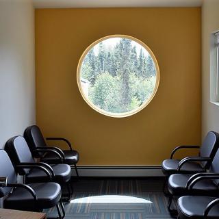 A modern waiting room with black chairs and a large circular window letting in natural light.