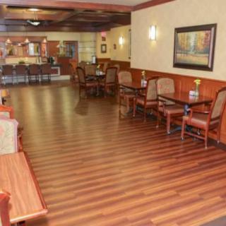 A cozy restaurant dining area with wooden floors, tables, and chairs, softly lit by wall lights.