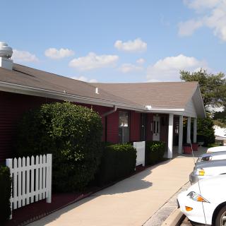 A one-story building with a sidewalk and parked cars under a partly cloudy sky.
