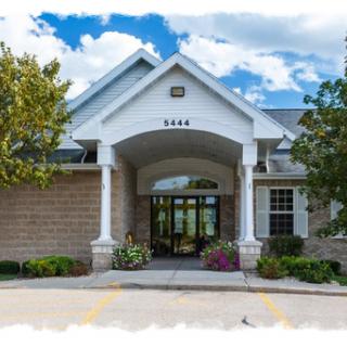 A welcoming entrance of a modern building framed by lush landscaping against a partly cloudy sky.