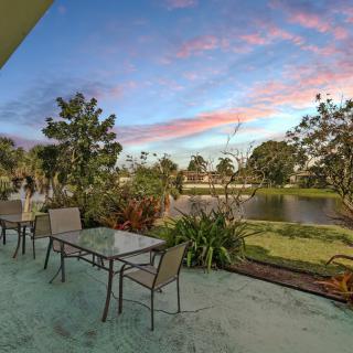 A scenic patio view with chairs and tables overlooking a garden and lake at sunset.
