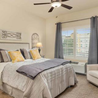 A cozy bedroom with a neatly made bed, decorative pillows, and a ceiling fan.