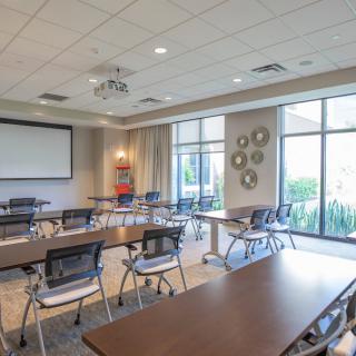 A bright and spacious conference room featuring tables, chairs, and a projector screen.