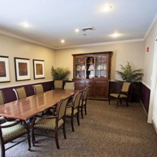 A well-appointed meeting room with a long wooden conference table surrounded by chairs, featuring decorative plants and framed artwork on the walls.