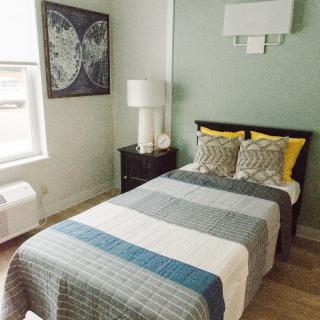 A cozy bedroom featuring a neatly made bed with patterned pillows, a bedside table with a lamp, and artwork on the wall.
