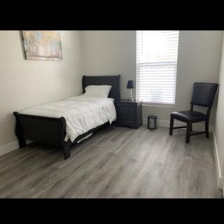 A minimalist bedroom with a single bed, nightstand, lamp, and chair.