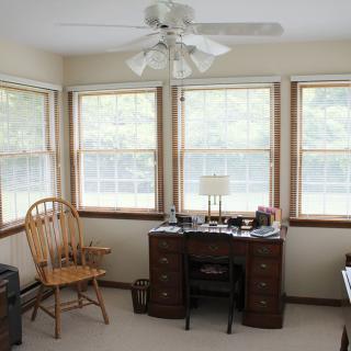 A cozy home office with a wooden desk, chair, and large windows providing natural light.